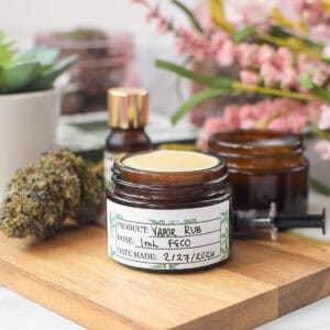 Cannabis-infused vapor rub jar with herbs and essential oils on wooden surface.