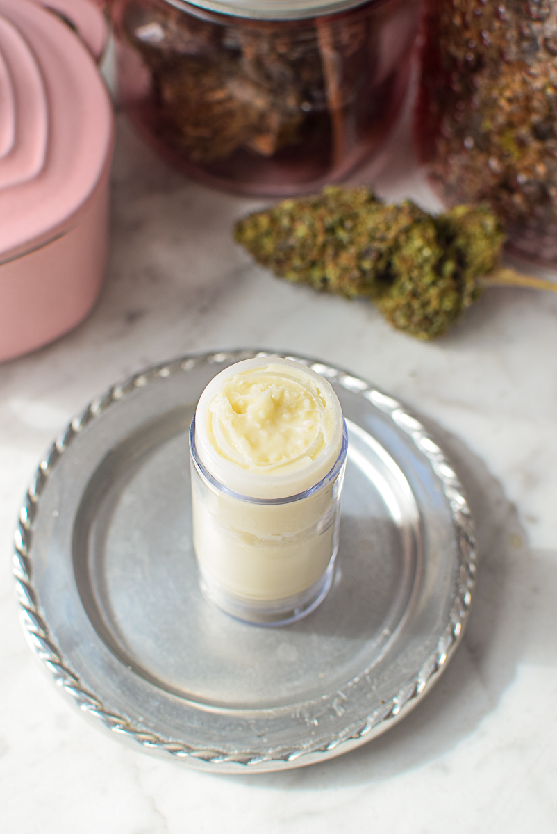 Homemade cannabis-infused balm in a small glass jar on a silver tray.