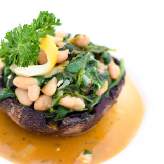 If you love garlic and lemon, this recipe is for you! Tender kale and white beans sauteed with lemon and garlic stuffed inside a baked portabella mushroom cap make this a perfect Meatless Meal! | @EmKyleNutrition