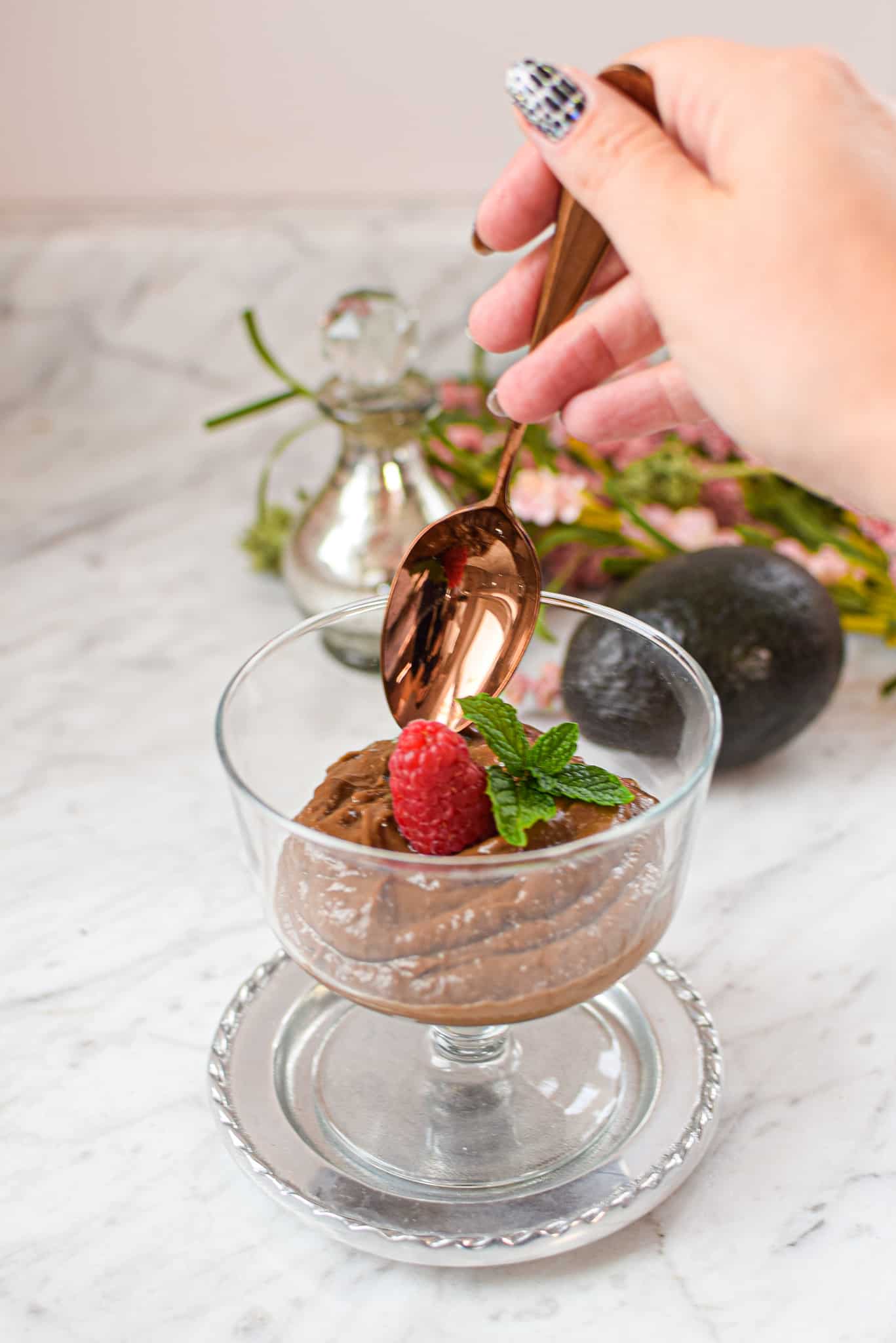 A picture of a clear trifle glass full of cannabis raspberry chocolate pudding with a spoon getting put in it.