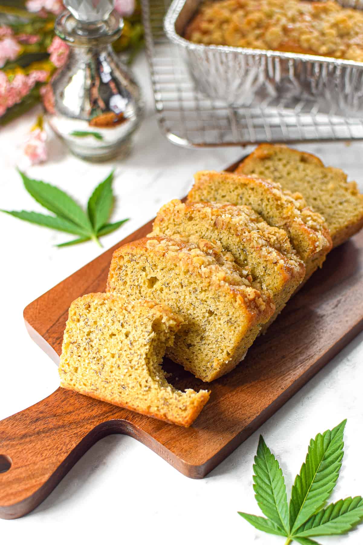 A photo of sliced cannabis banana bread on a cutting board with a cannabis leaf in the background