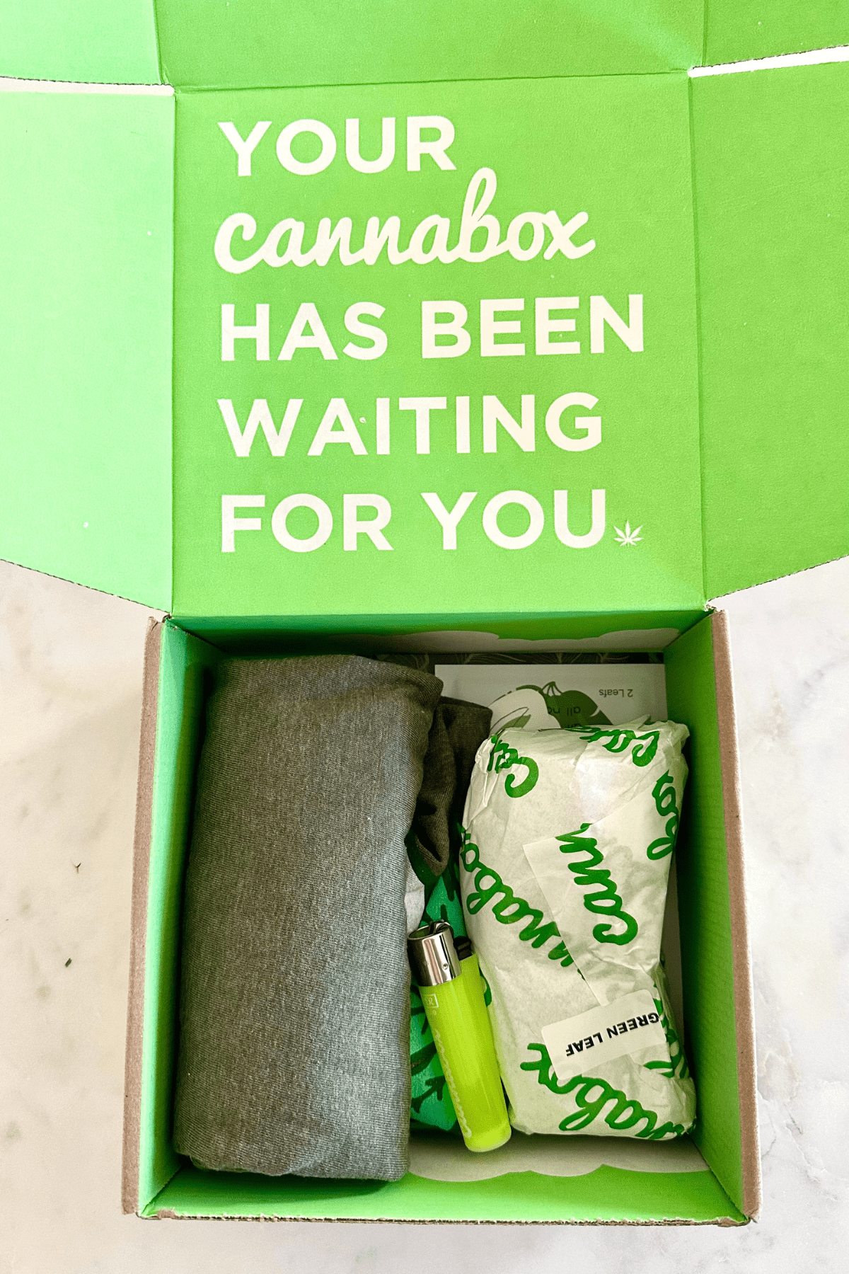 A picture of a cannabox open with items like a lighter and a shirt inside.