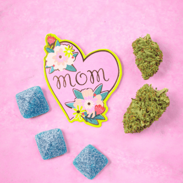 A picture of a pink background with blue bliss gummies, cannabis flower, and a sign that says mom.