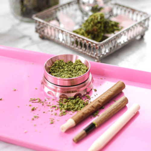 A picture of a pink rolloing try with cannabis and a blunt.