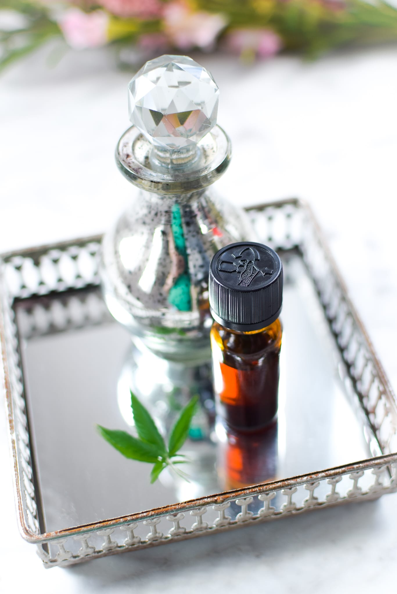 A white countertop with a metal tray with a amber tincture bottle with cannabis to the lefthand side, ever clear bottle in the background