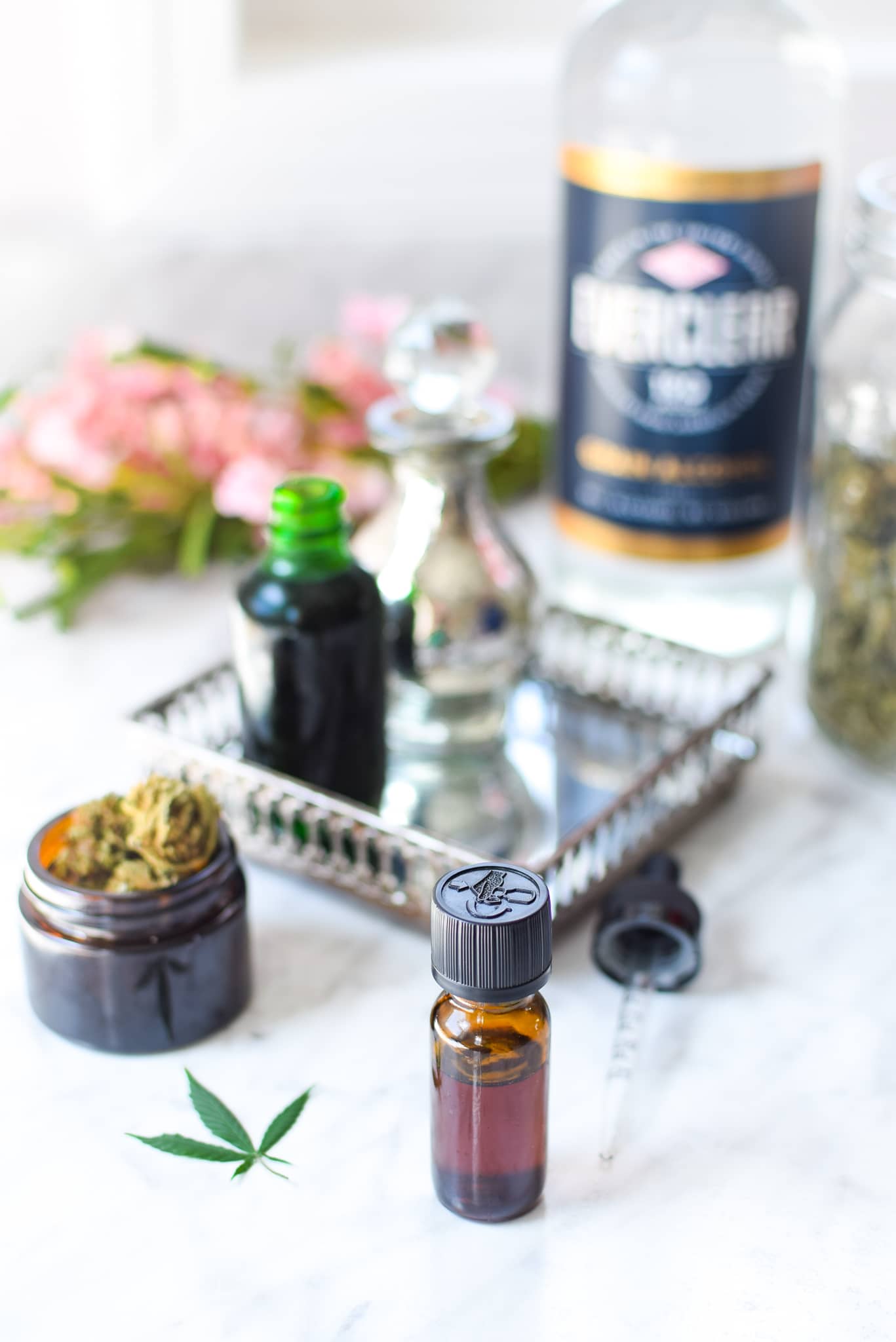 A white countertop with a metal tray with a amber tincture bottle with cannabis to the lefthand side, ever clear bottle in the background