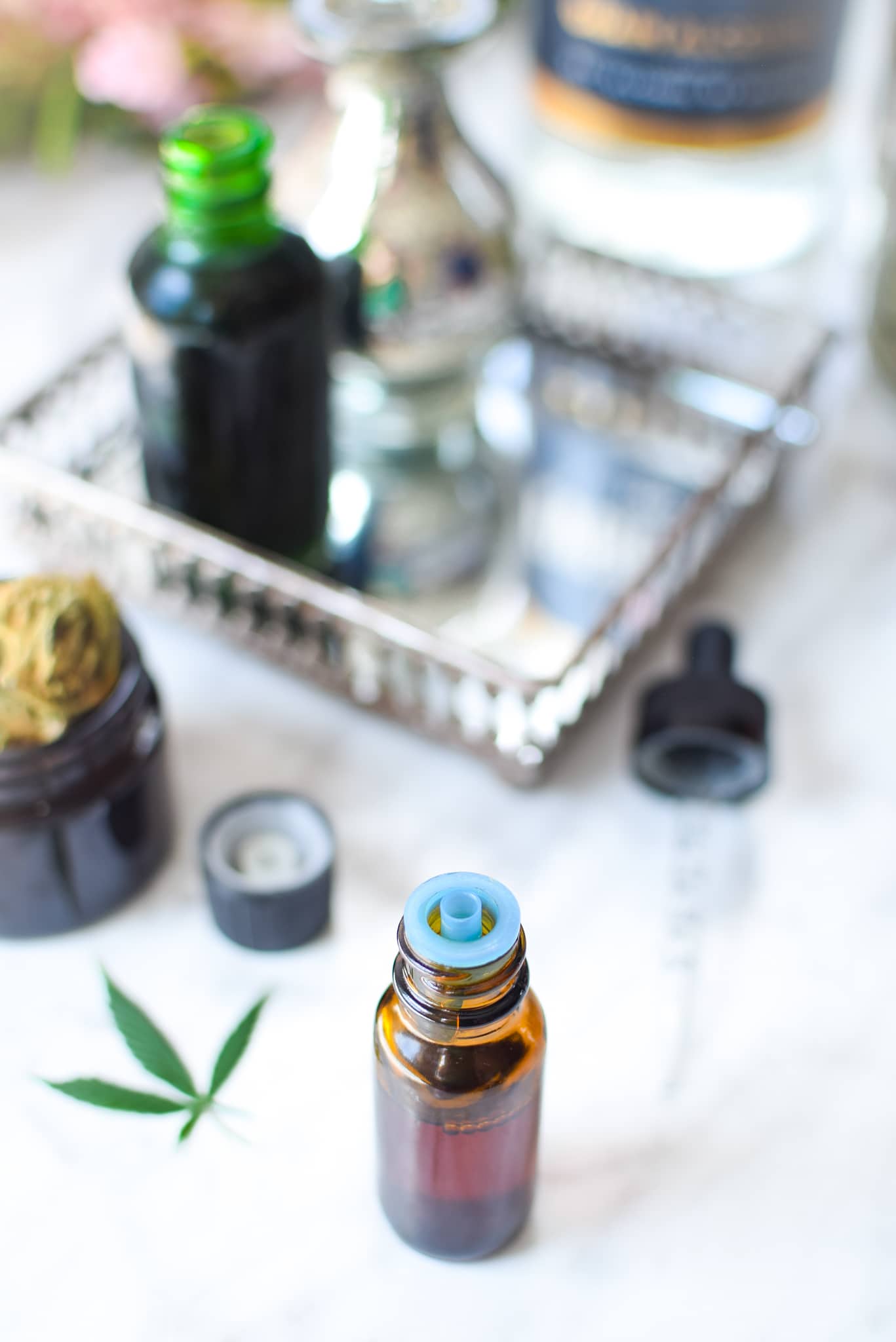 A white countertop with a metal tray with a amber tincture bottle with cannabis to the lefthand side, ever clear bottle in the background