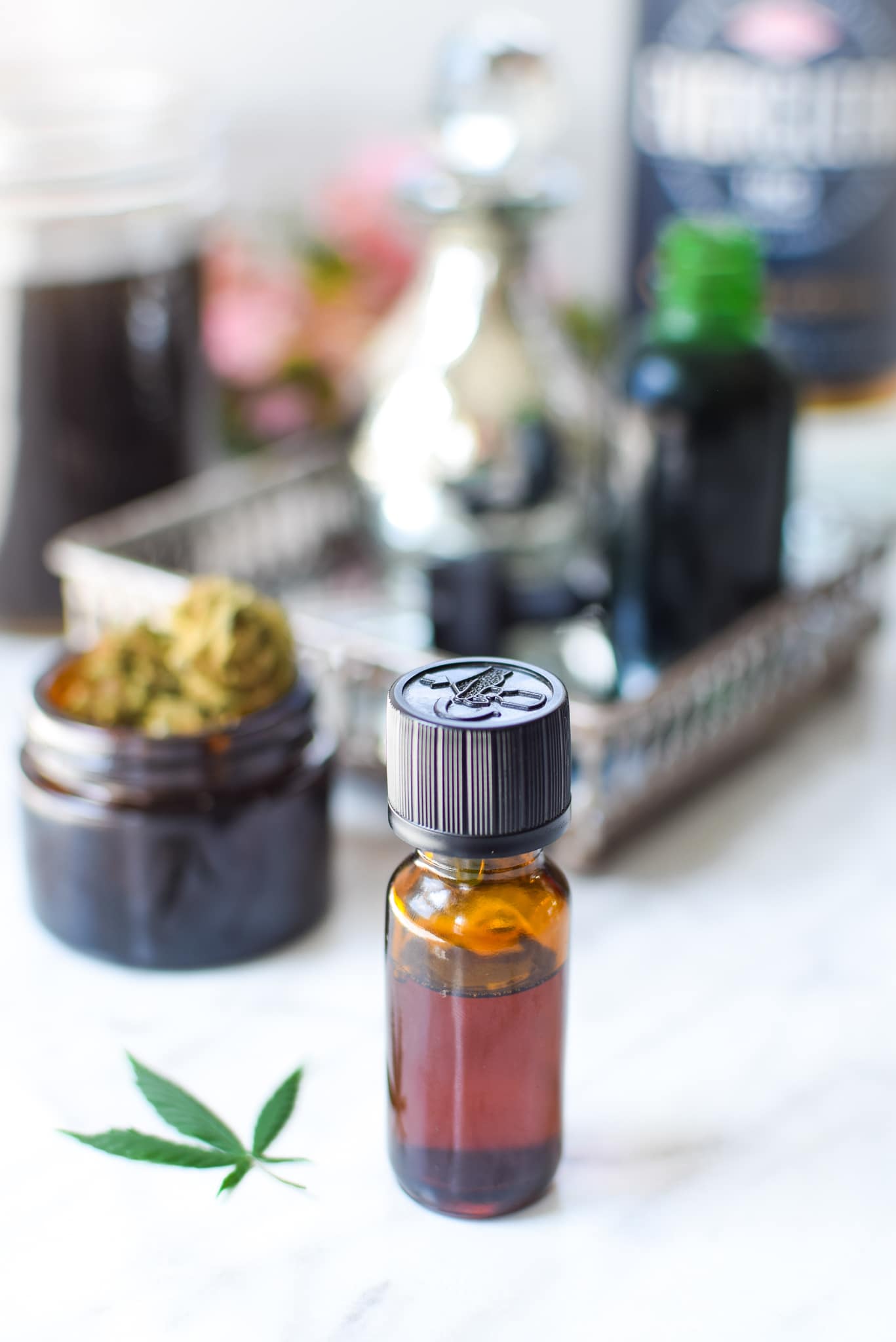 A white countertop with a metal tray with a amber tincture bottle with cannabis to the lefthand side, ever clear bottle in the background