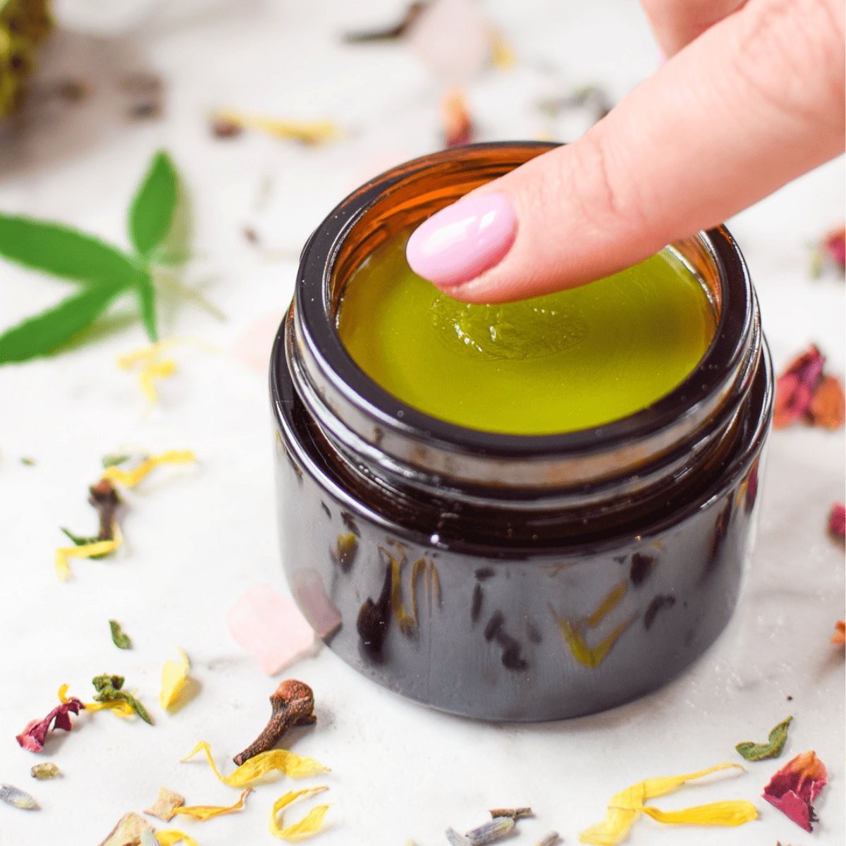 A picture of a hand in a jar of cannabis salve.