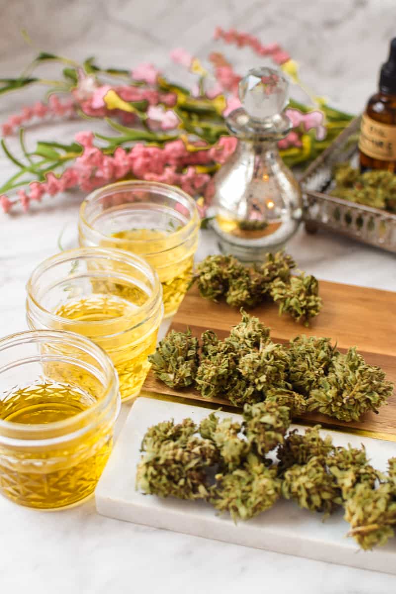 A white countertop with three jars or oil with different amounts of cannabis next to each jar. 