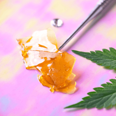 A picture of a pink background with a cannabis concentrate and a cannabis leaf.