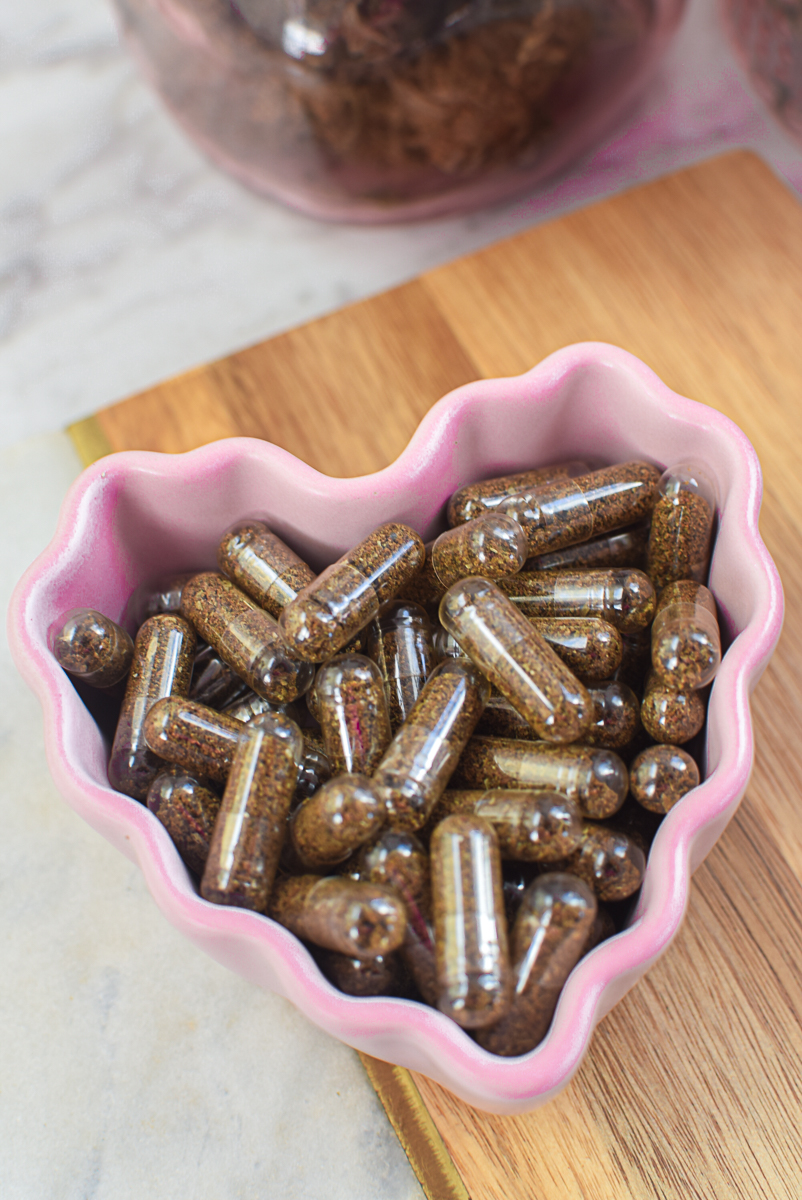 Cannabis capsules in a pink heart-shaped dish with cannabis buds and dropper.