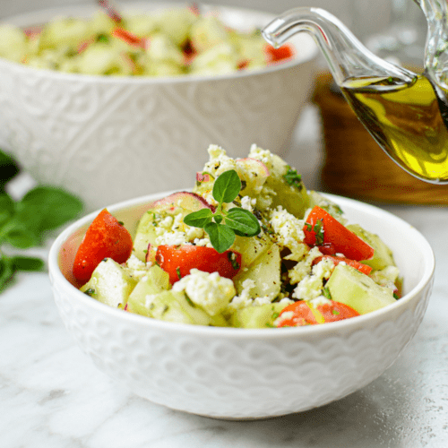 A white counter with a white bowl full of Cannabis-Infused Tomato Cucumber salad