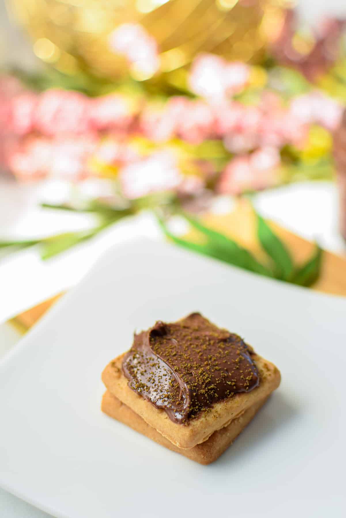 Small square cookies topped with Nutella topped with decarbed cannabis on a white plate.