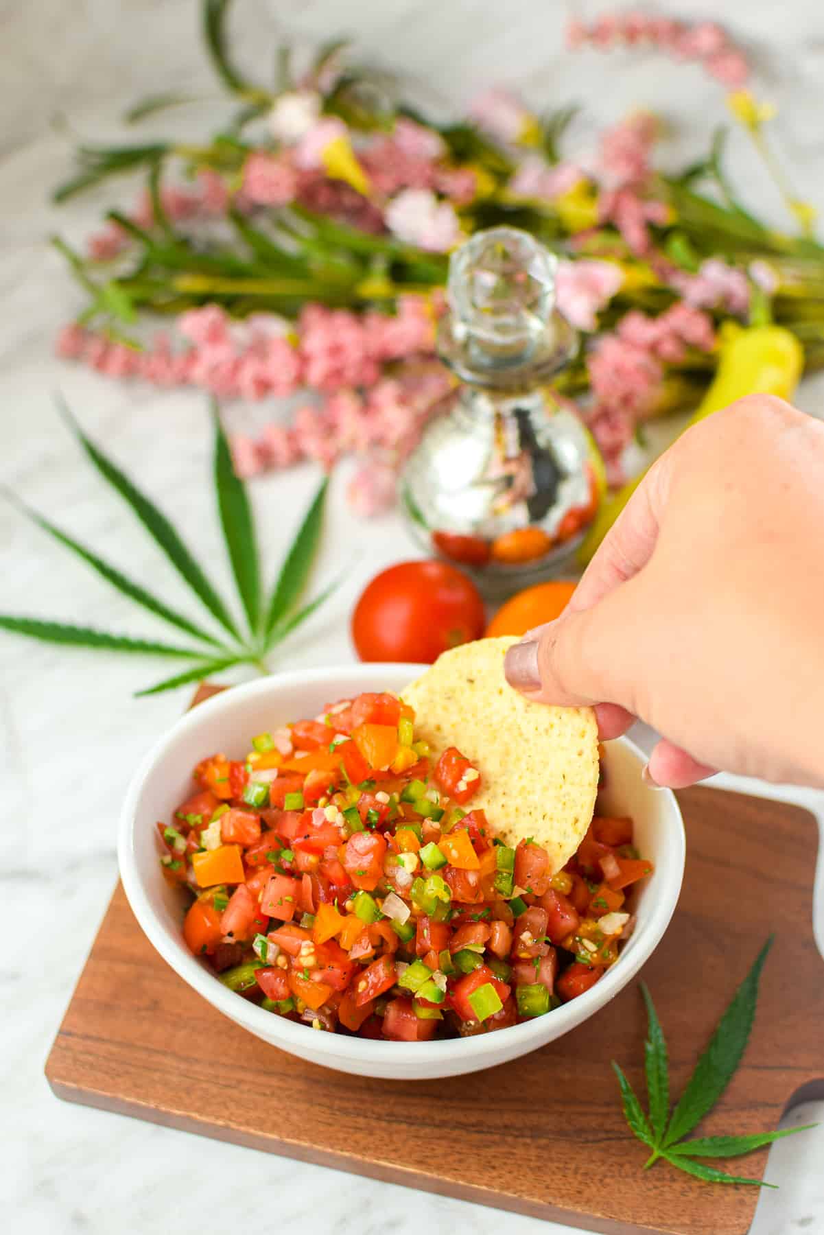 A finished bowl of cannabis infused salsa with a hand dipping a chip in