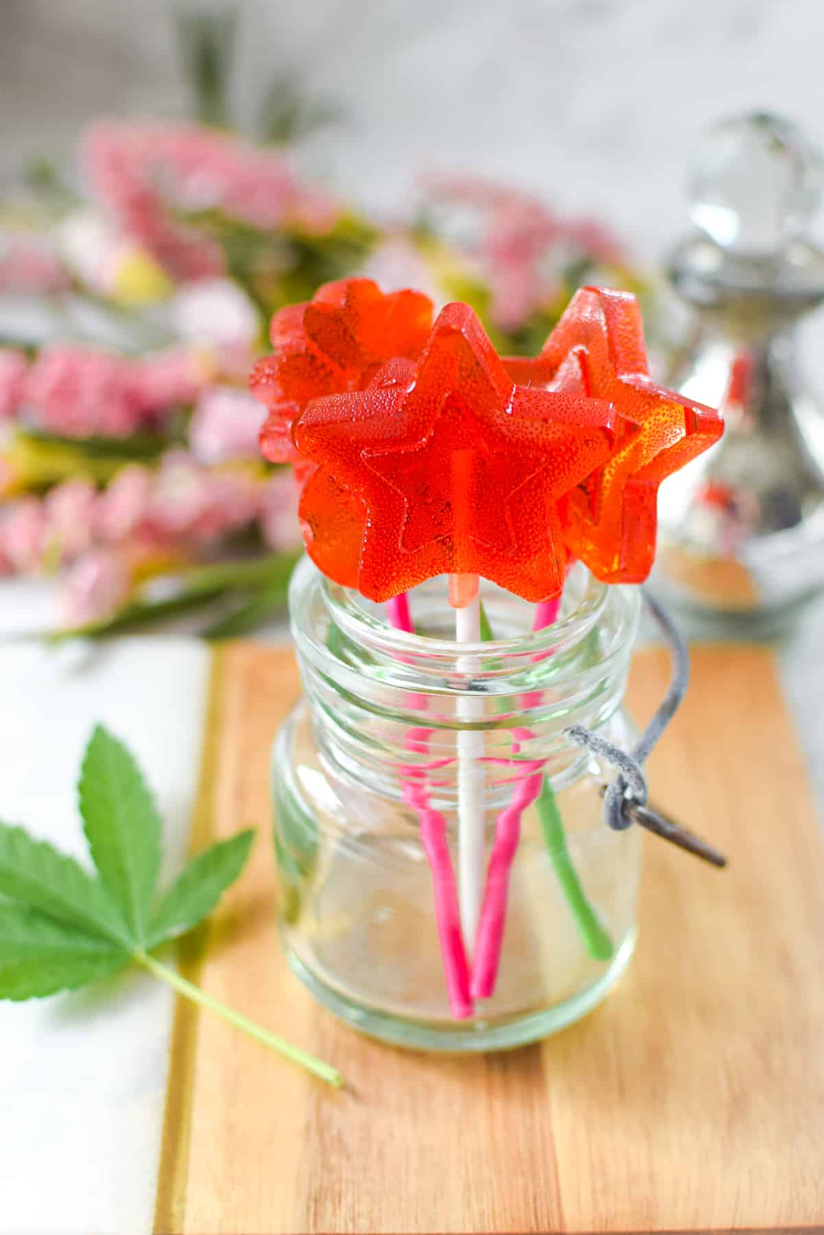 A wooden cutting board with a small mason jar full of red cannabis lollipops
