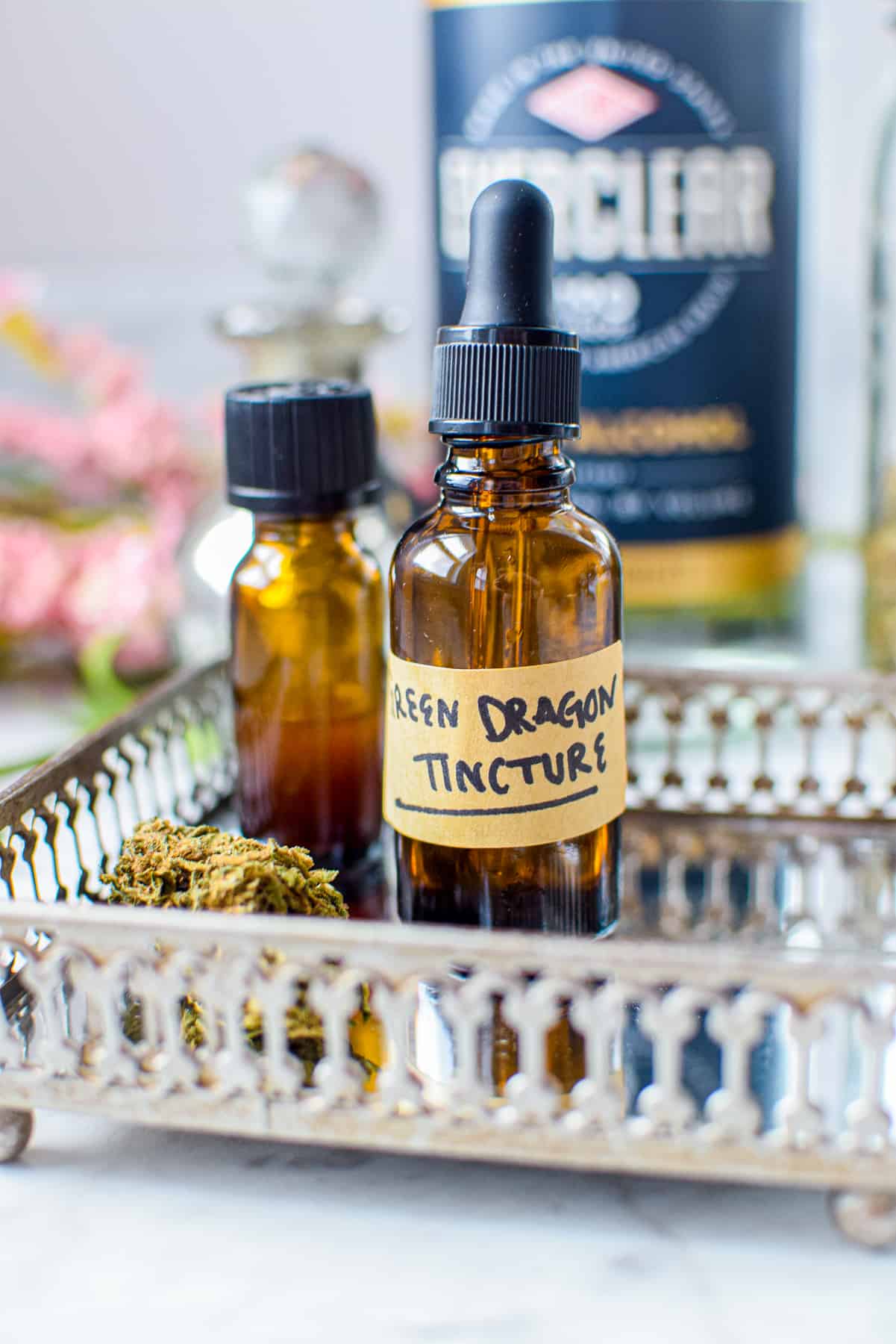 A white countertop with a metal tray with a amber tincture bottle labeled green dragon tincture with cannabis to the lefthand side, ever clear bottle in the background