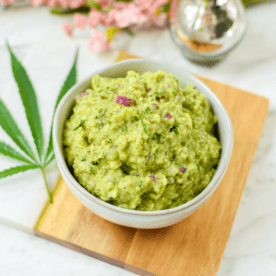 A bowl filled with guacamole garnished with a cannabis leaf