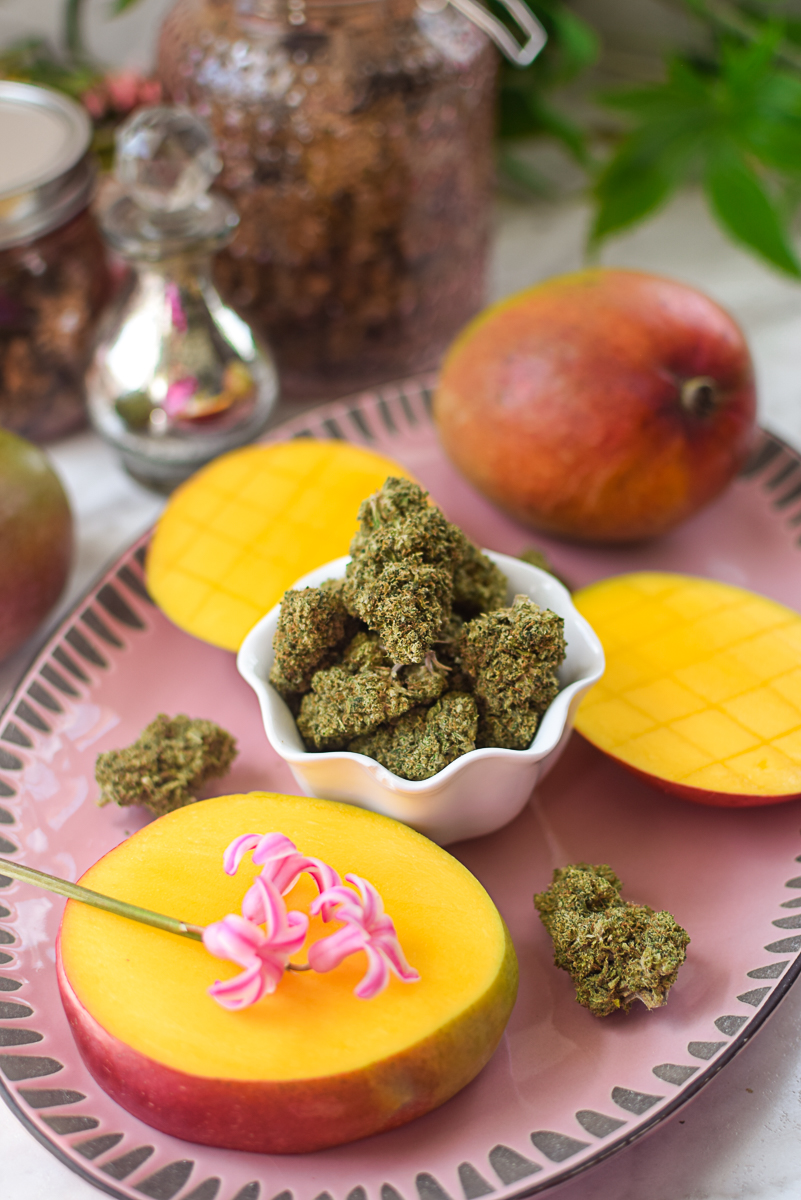 A picture of a mango and cannabis flower on a pink countertop.