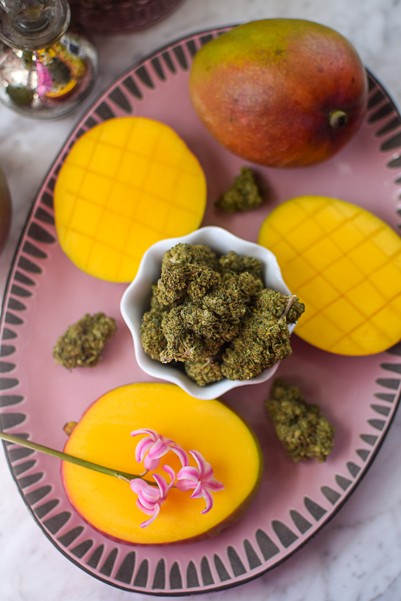 A picture of a mango and cannabis flower on a pink countertop.