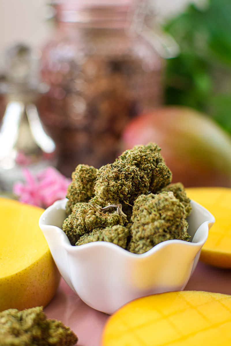 A picture of a mango and cannabis flower on a pink countertop.