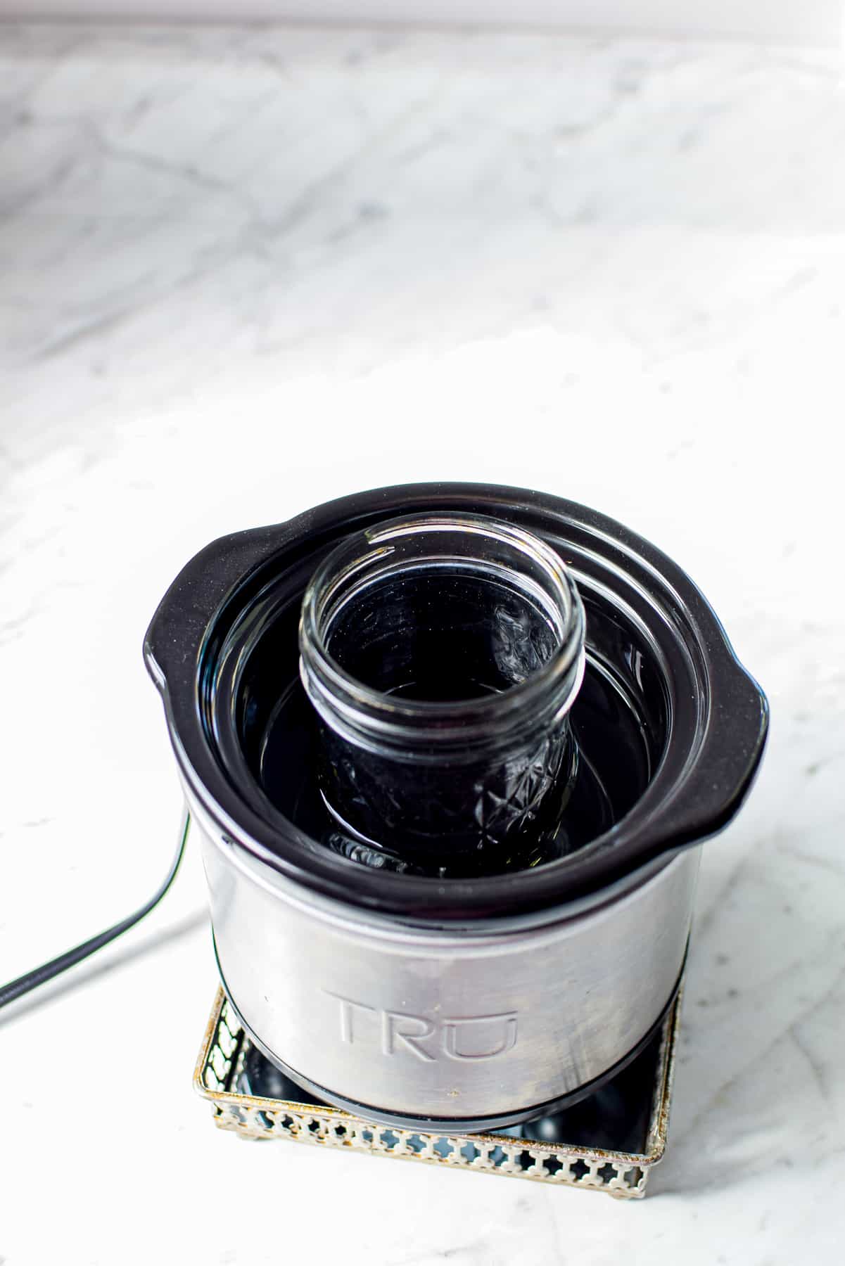 A white countertop with a small warming crockpot with a mini mason jar inside