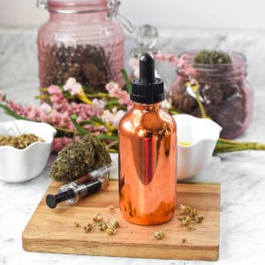 Copper dropper bottle with CBD oil for glowing skin, surrounded by herbs and flowers.