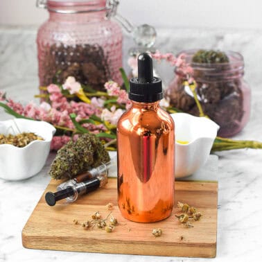 Copper dropper bottle with CBD oil for glowing skin, surrounded by herbs and flowers.