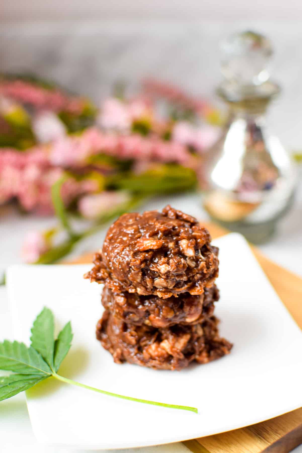 A white countertop with a cutting board topped with a white plate topped with three no-bake rocky road cannabis cookies