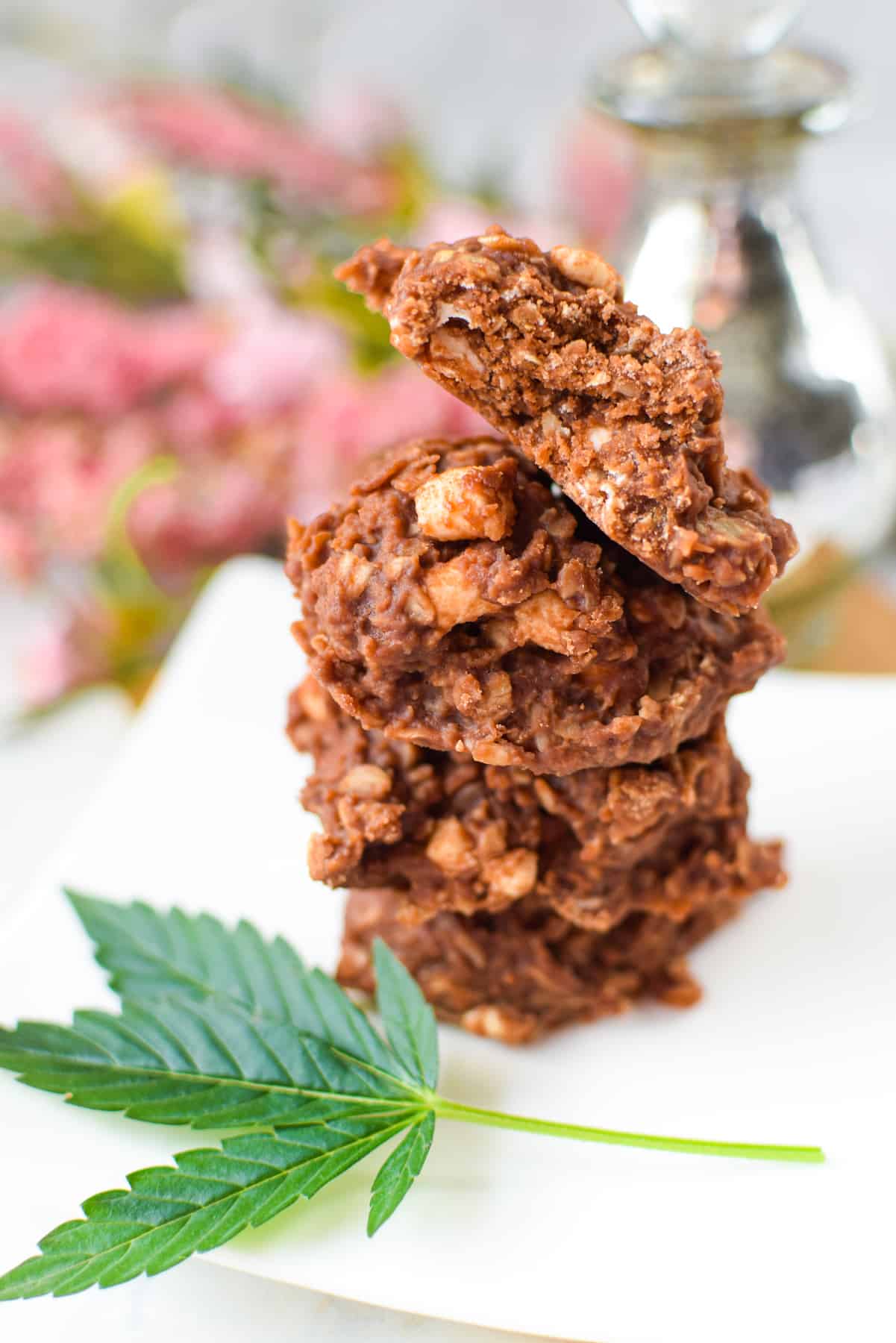 A white countertop with a cutting board topped with a white plate topped with three no-bake rocky road cannabis cookies