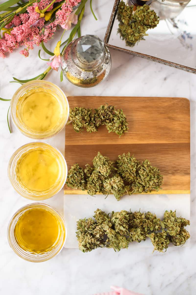 A white countertop with three jars or oil with different amounts of cannabis next to each jar. 