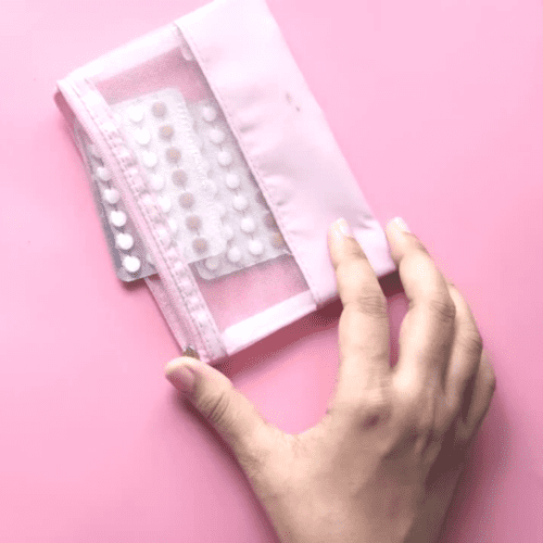 A pink background with a hand holding cannabis pills.