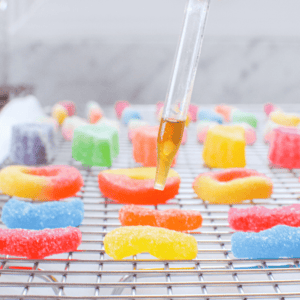 A white countertop with sugar coated gummies with a hand holding a dropper from above dropping tincture on the gummyuntertop with sugar coated gummies with a hand holding a dropper from above dropping tincture on the gummy