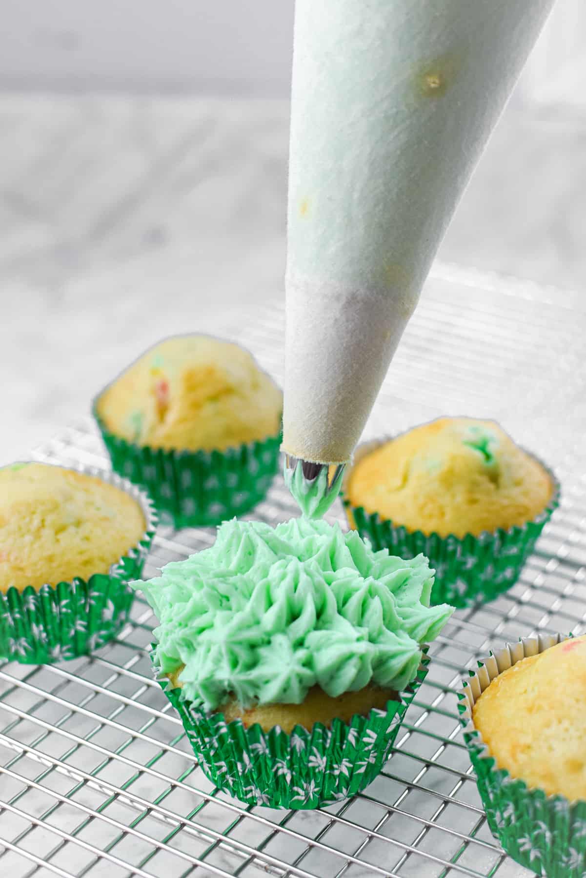 A white countertop with a cutting board and a cannabis cupcake topped with green frosting