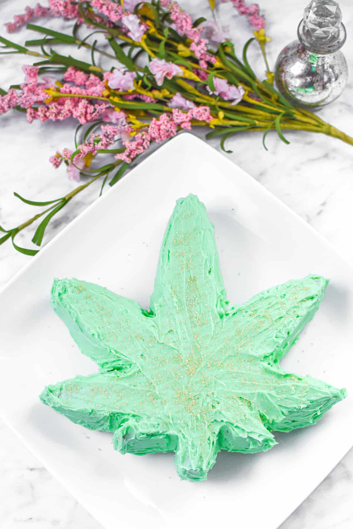 A white countertop with a white plate with a green cannabis cake on top.