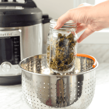 A picture of a hand placing a jar of cannabis inside an Instant pot for decarboxylation.