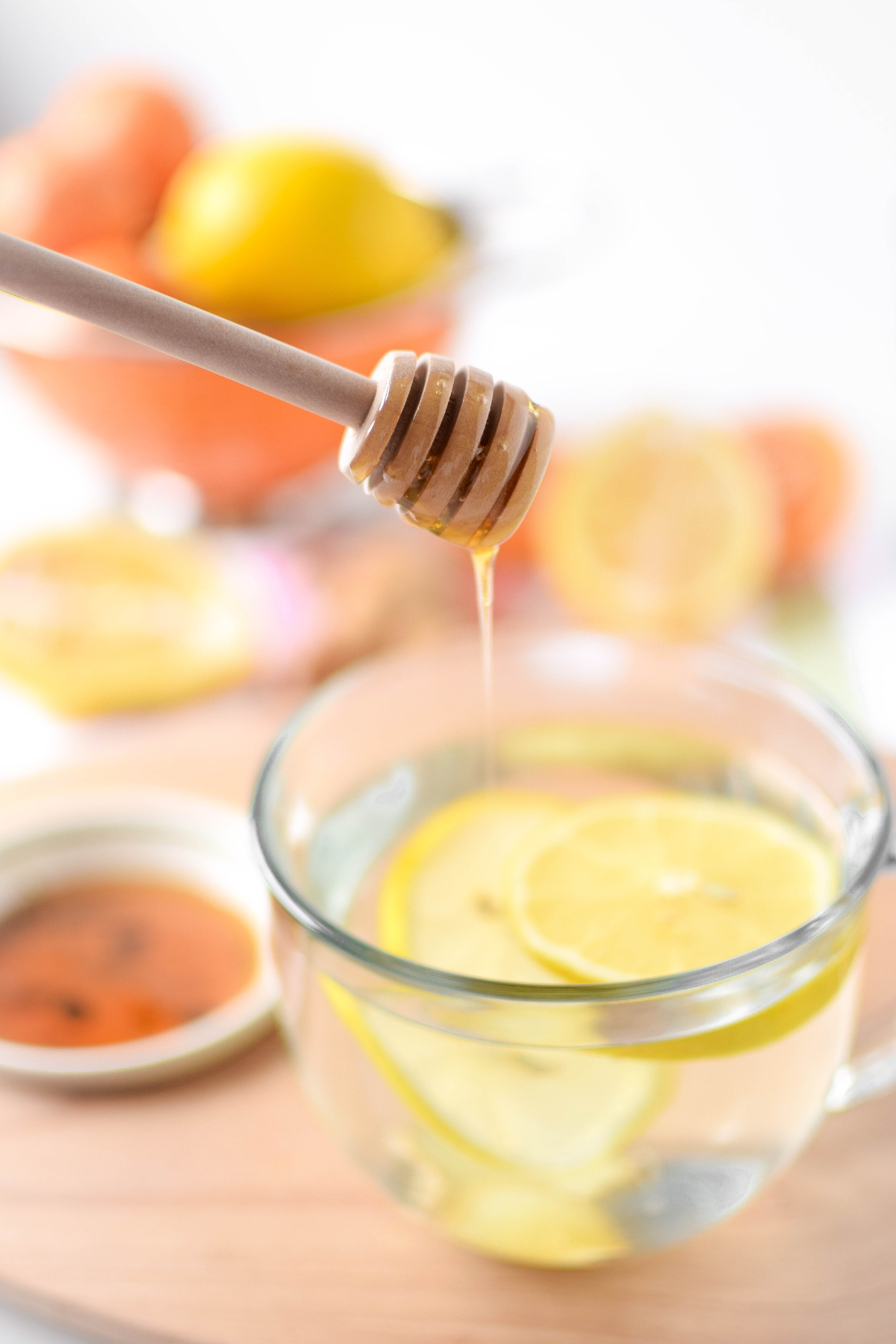 A picture of a clear mug full of lemon, ginger, and warm water with a honey dobber.