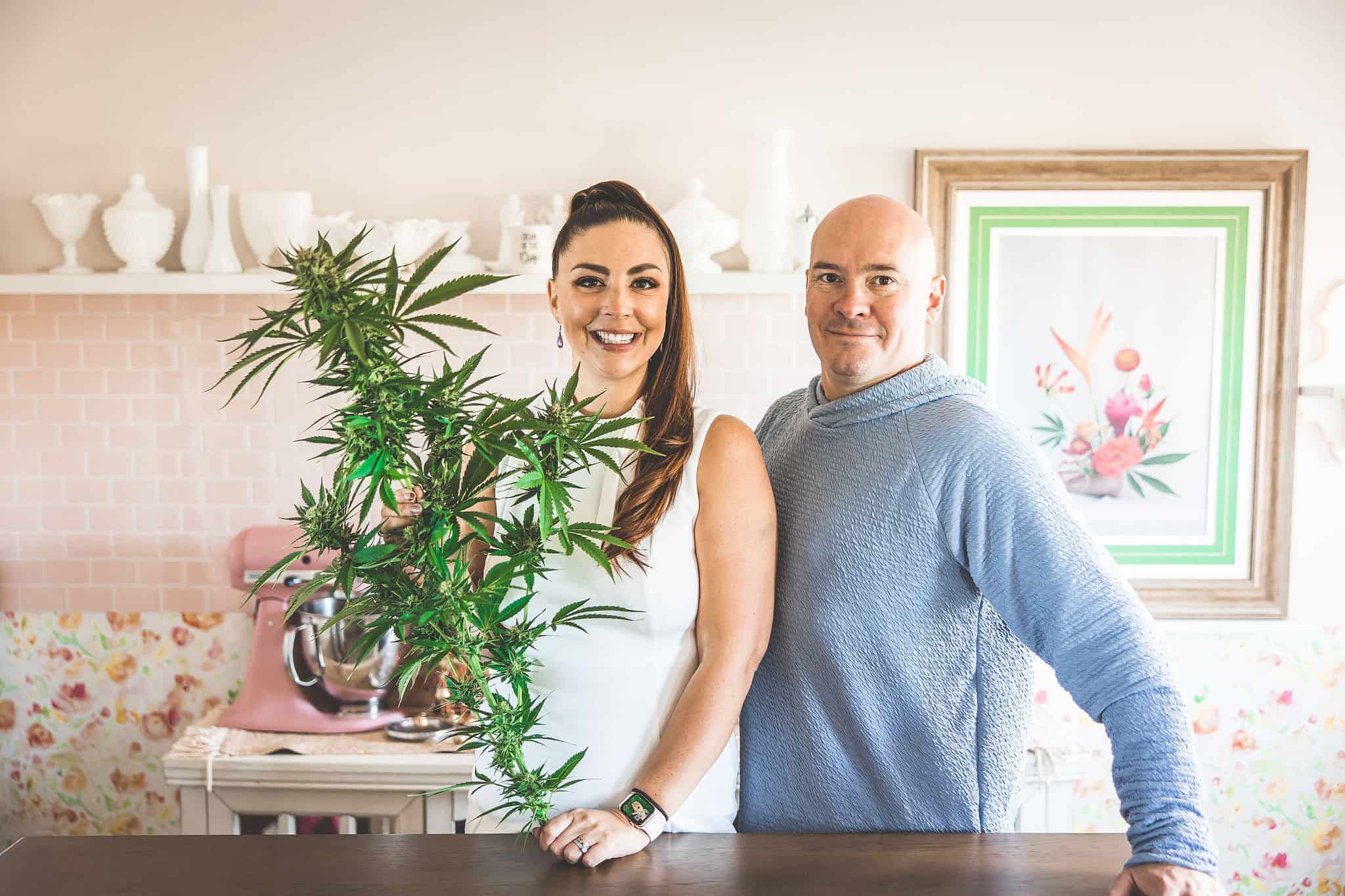 A picture of Emily and Phil Kyle in a pink kitchen holding a cannabis plant. 