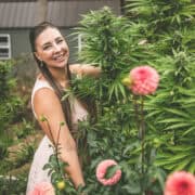 A picture of Emily Kyle in her garden with cannabis plants and dahlias.