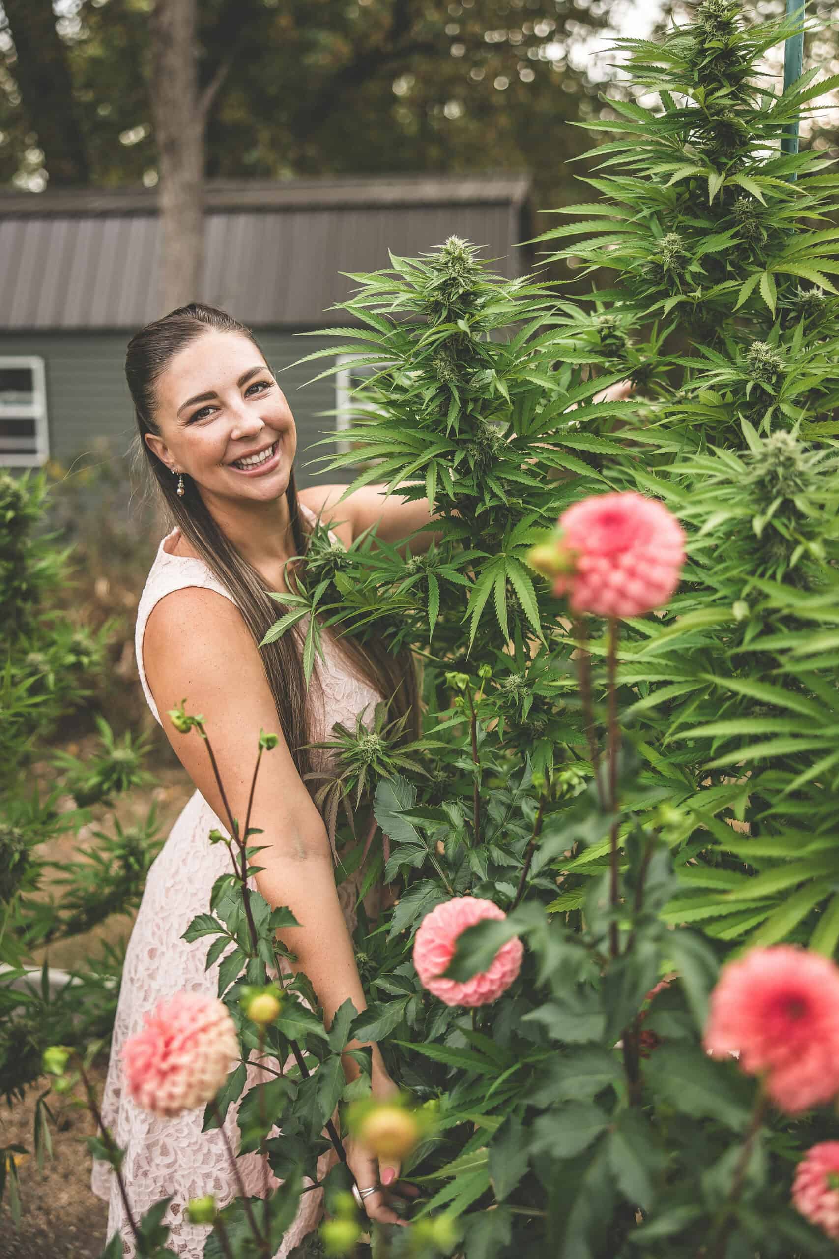 A picture of Emily Kyle in her garden with cannabis plants and dahlias.
