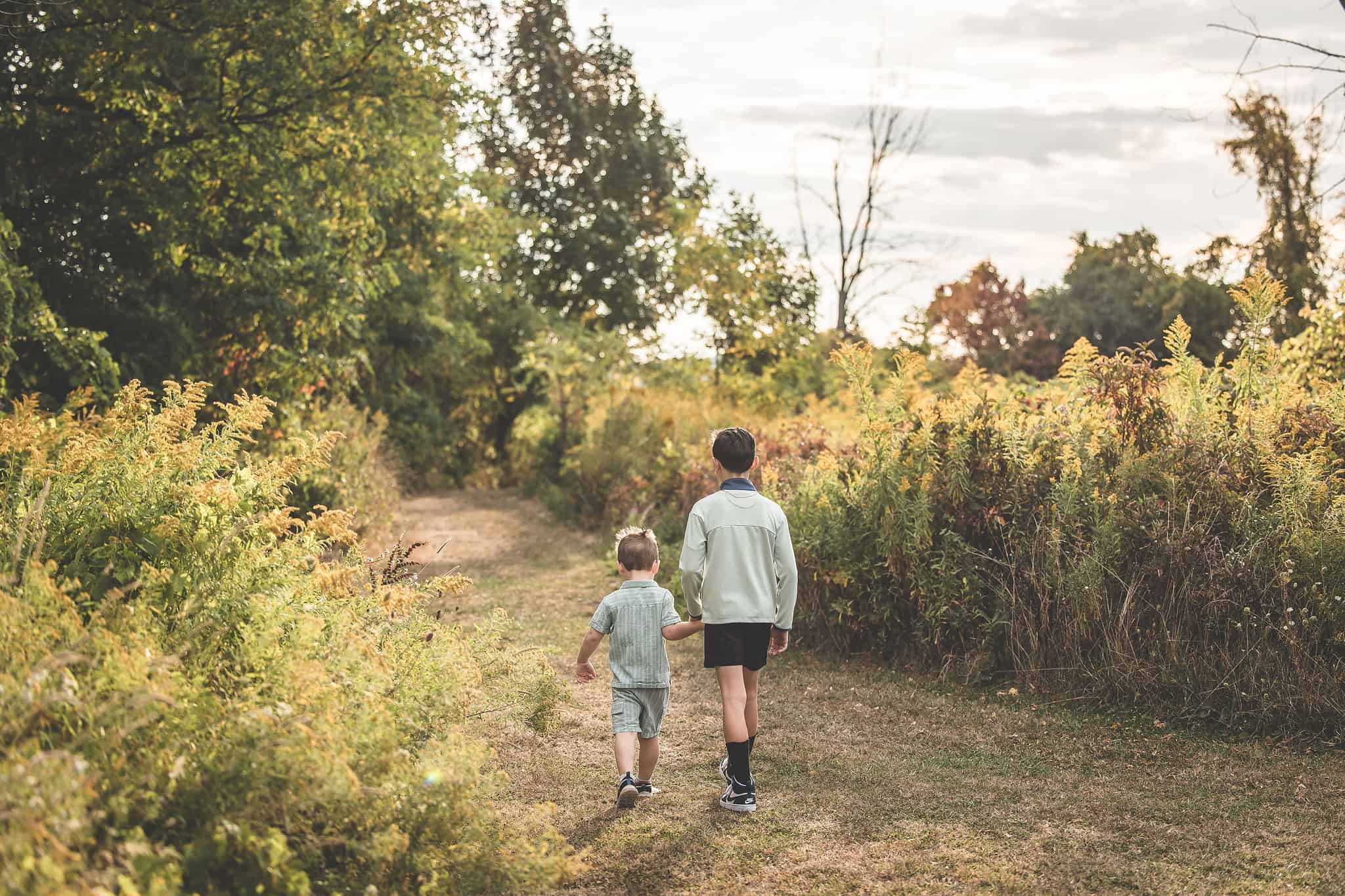 Reflective outdoor scene with children walking hand-in-hand on a nature trail in autumn; healthy lifestyle and outdoor activity theme.