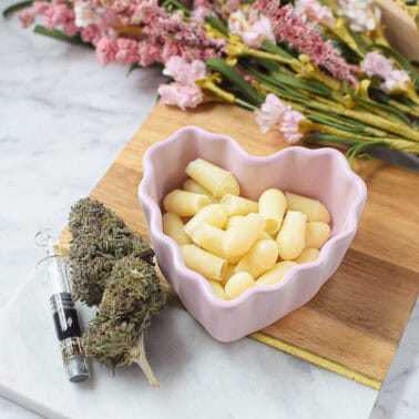 Cannabis suppositories in a pink bowl with herbs and syringe.