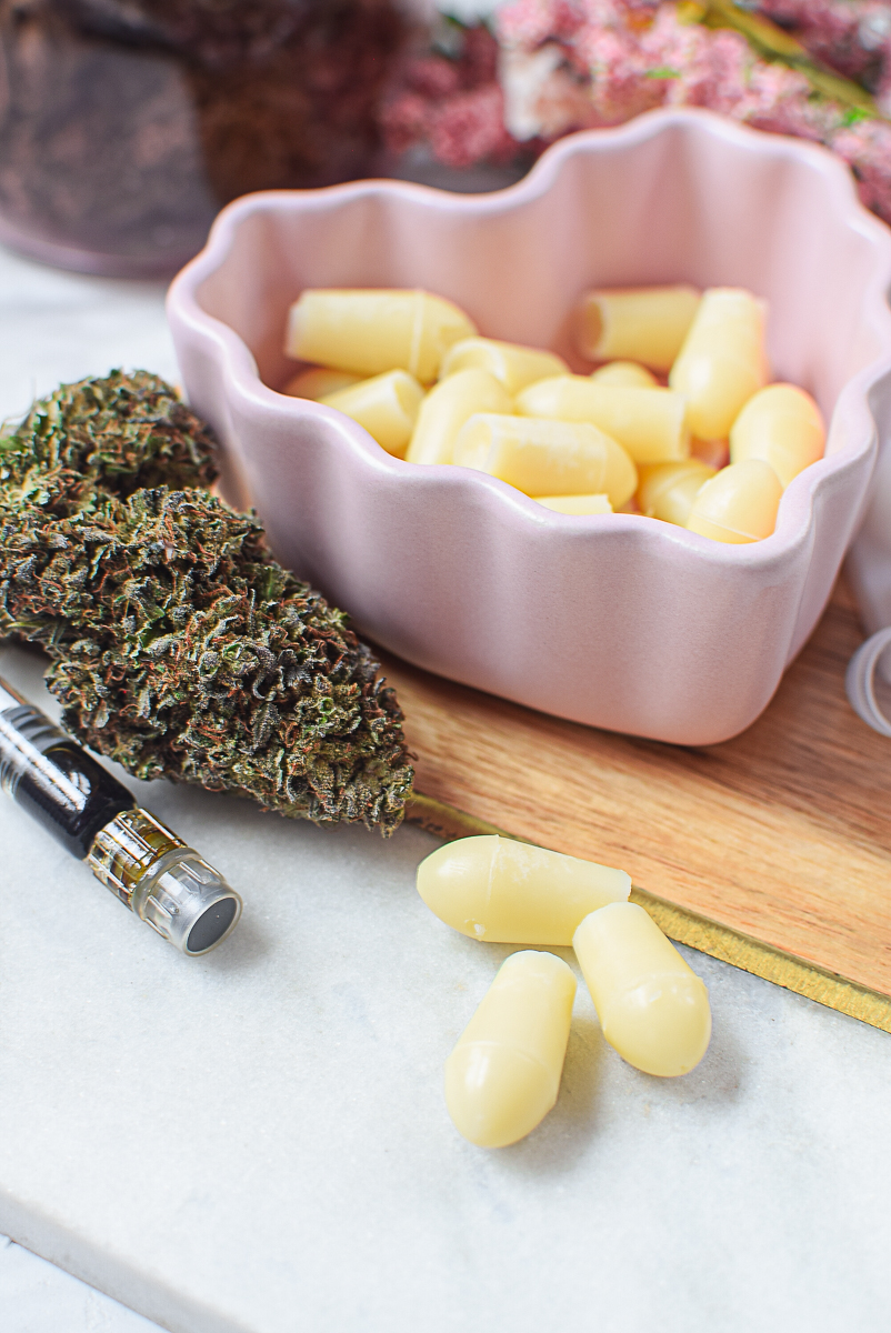 Cannabis suppository ingredients in a pink bowl with cannabis buds and capsules.