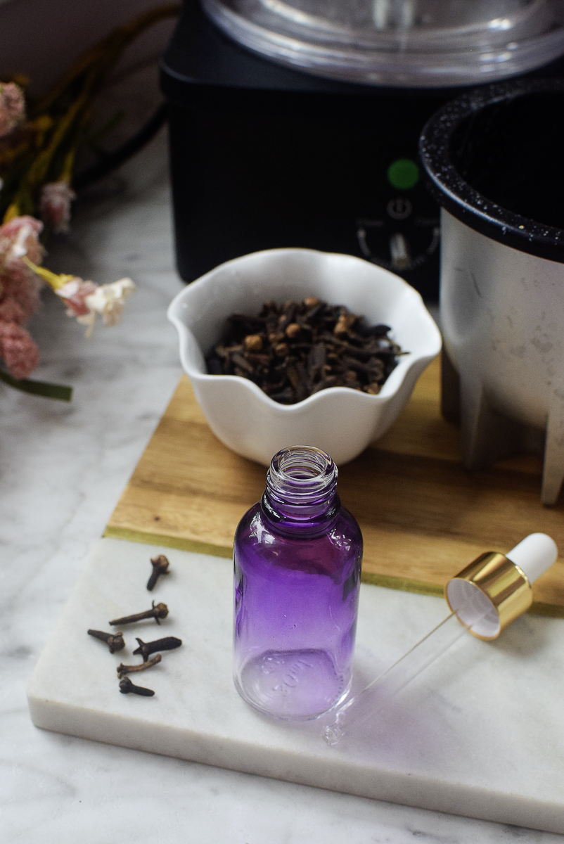 Open bottle of purple clove extract with dropper, a bowl of whole cloves, and the Source Turbo machine in the background