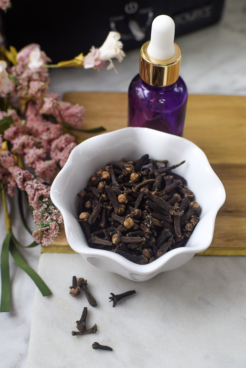 Purple glass dropper bottle of clove extract styled with dried flowers and whole cloves
