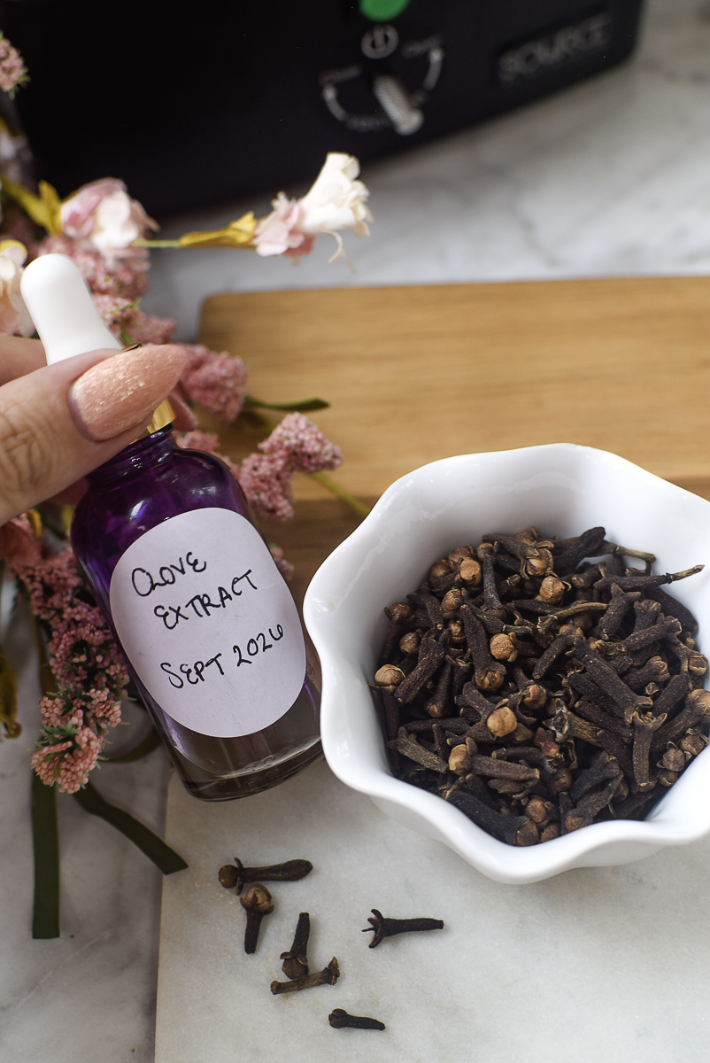 Hand holding a bottle labeled Clove Extract Sept 2026 next to a bowl of whole cloves