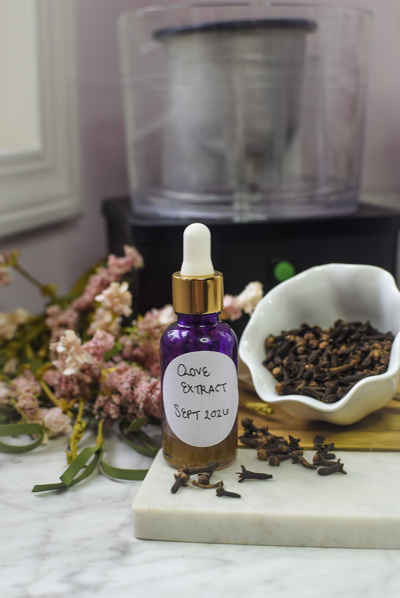 Dropper bottle of clove extract labeled Clove Extract Sept 2026 beside a bowl of whole cloves and dried flowers
