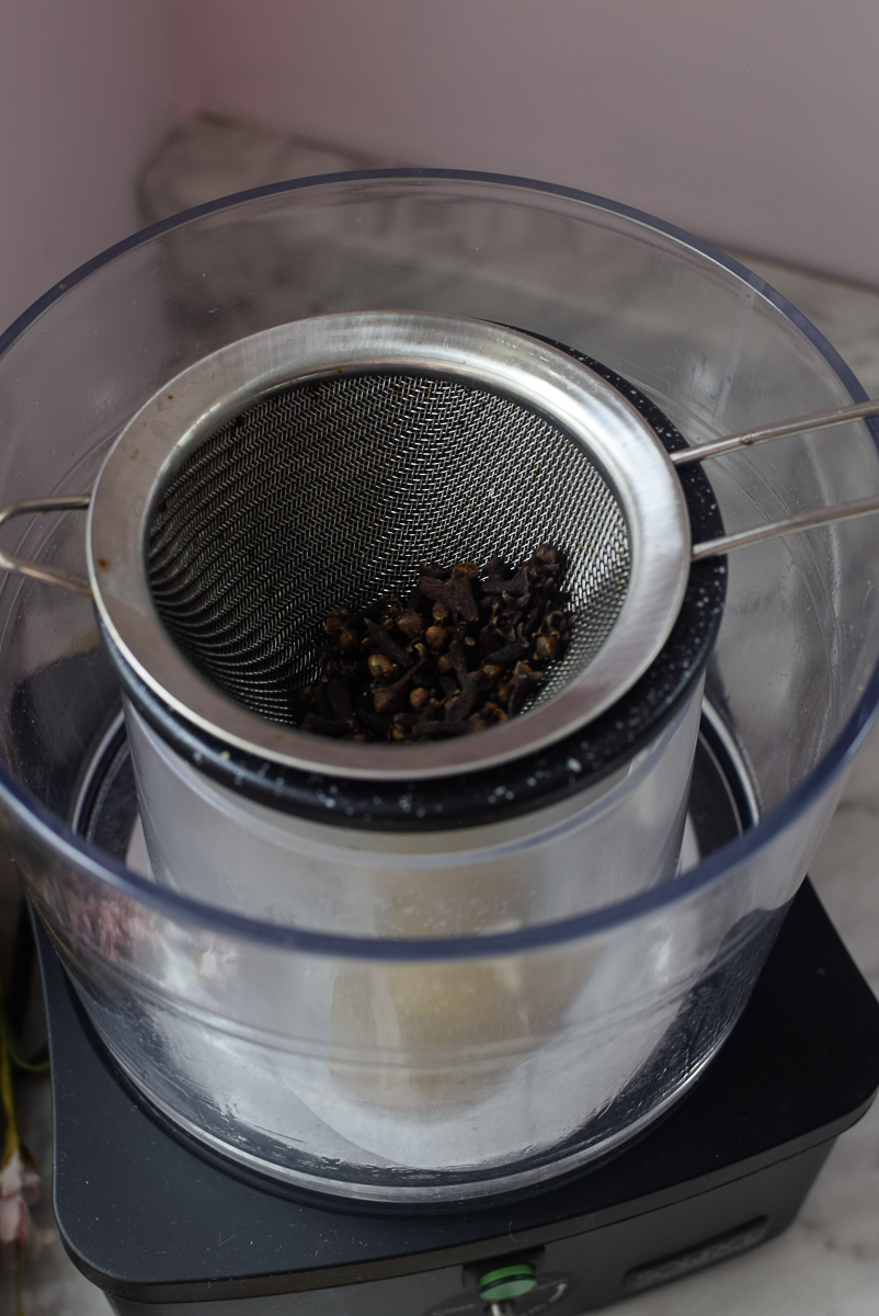 Whole cloves being strained through a fine mesh strainer into the Source Turbo container